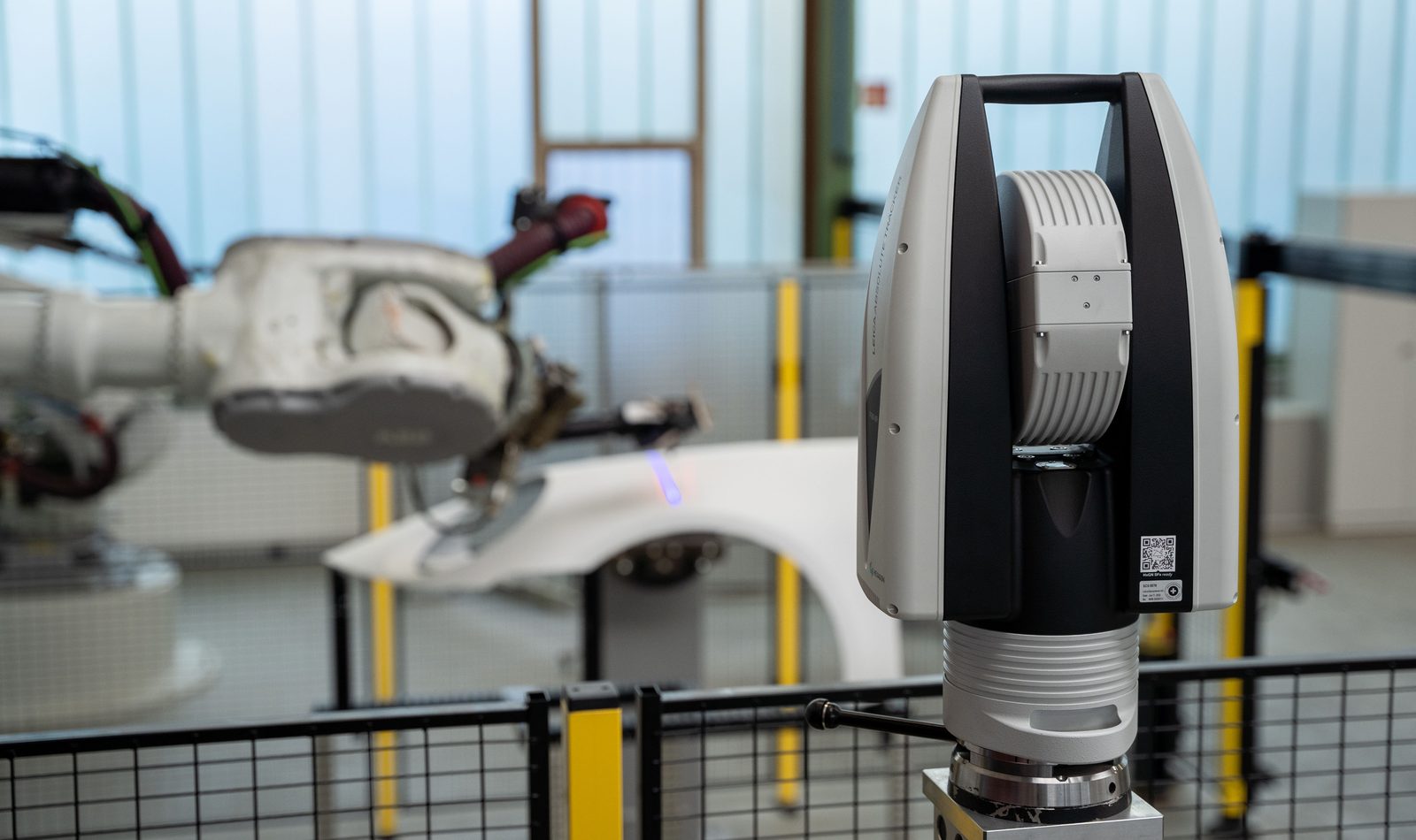 Hexagon AT960 Lasertracker vor einer Roboterzelle beim Scannen eines Karosserieteils